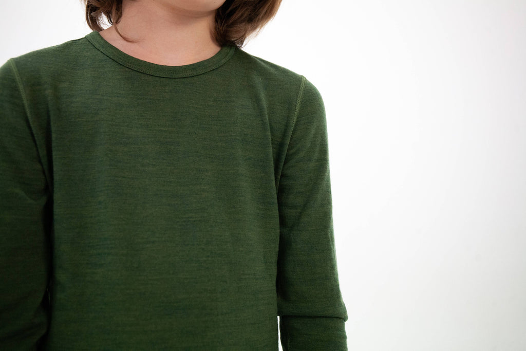 A close-up of a person wearing a dark olive green long-sleeve crewneck shirt against a plain white background.