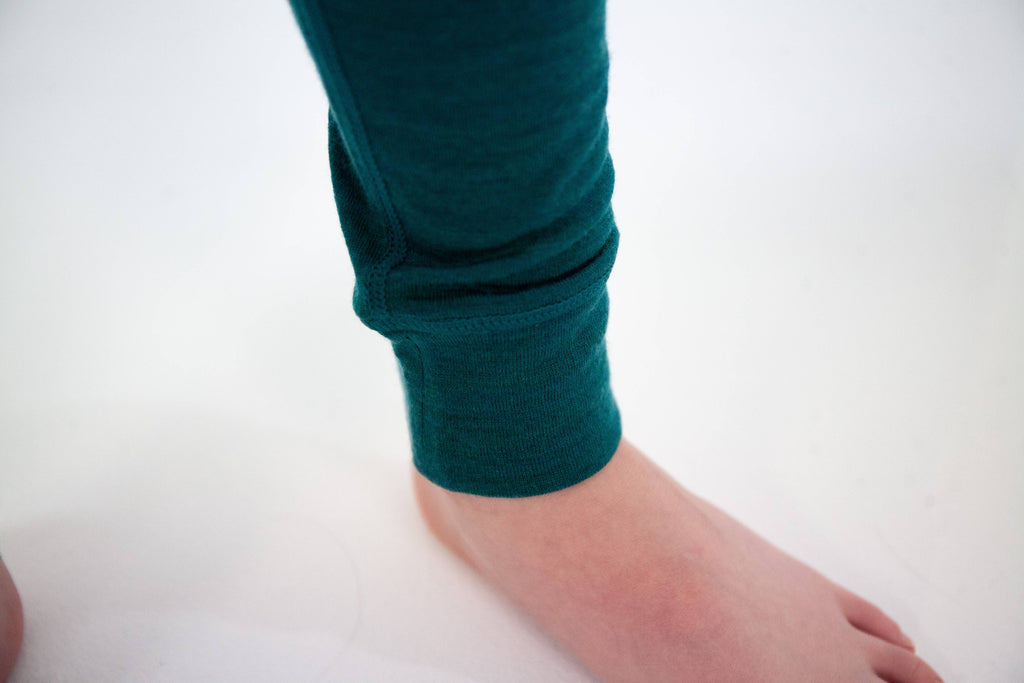 A close-up of a person's bare foot and ankle wearing a dark teal ribbed knit sock or pant leg cuff against a plain white background.