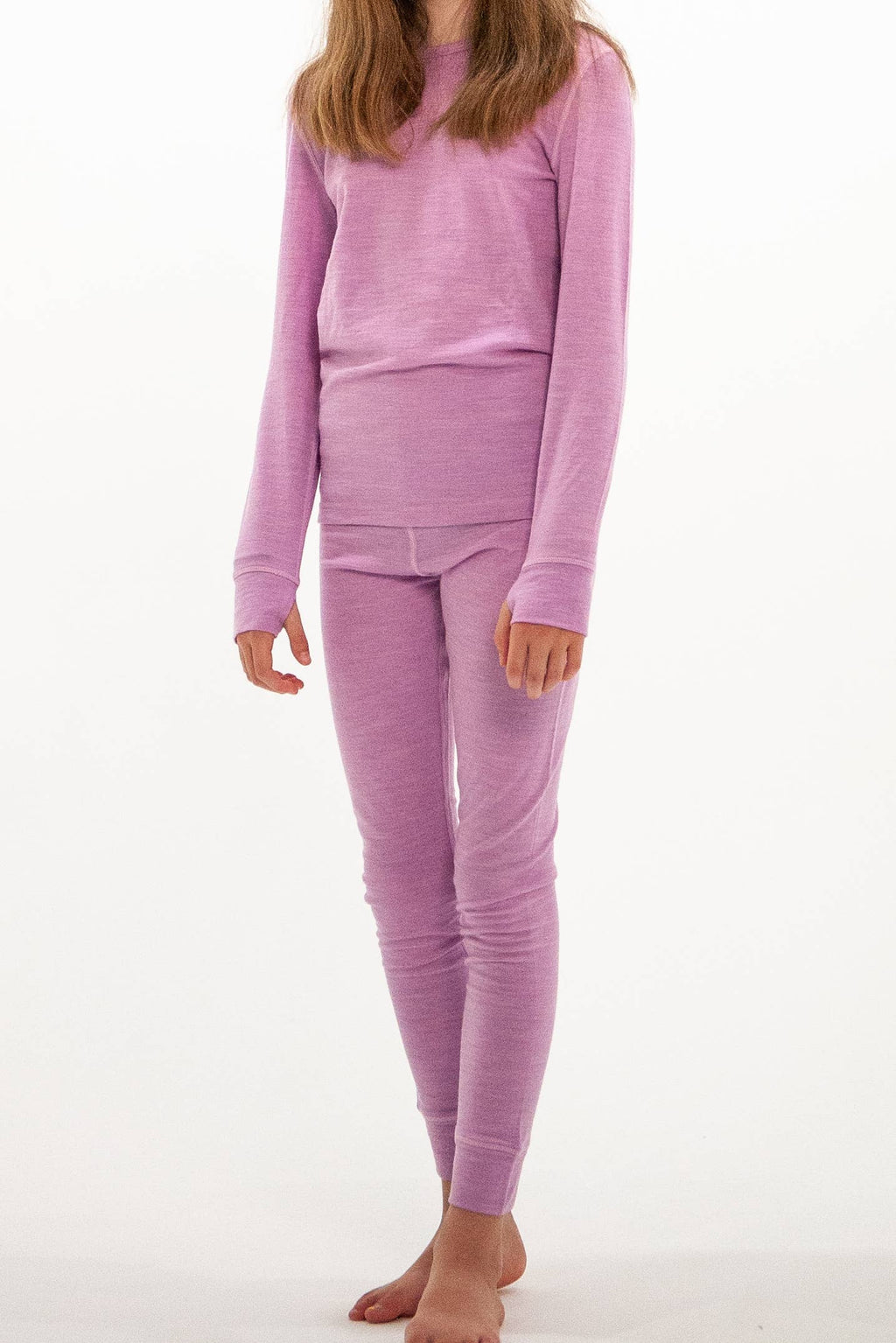 A child wearing a matching two-piece pajama set in a soft lavender-purple color, consisting of a long-sleeve top and leggings, standing against a plain white background.