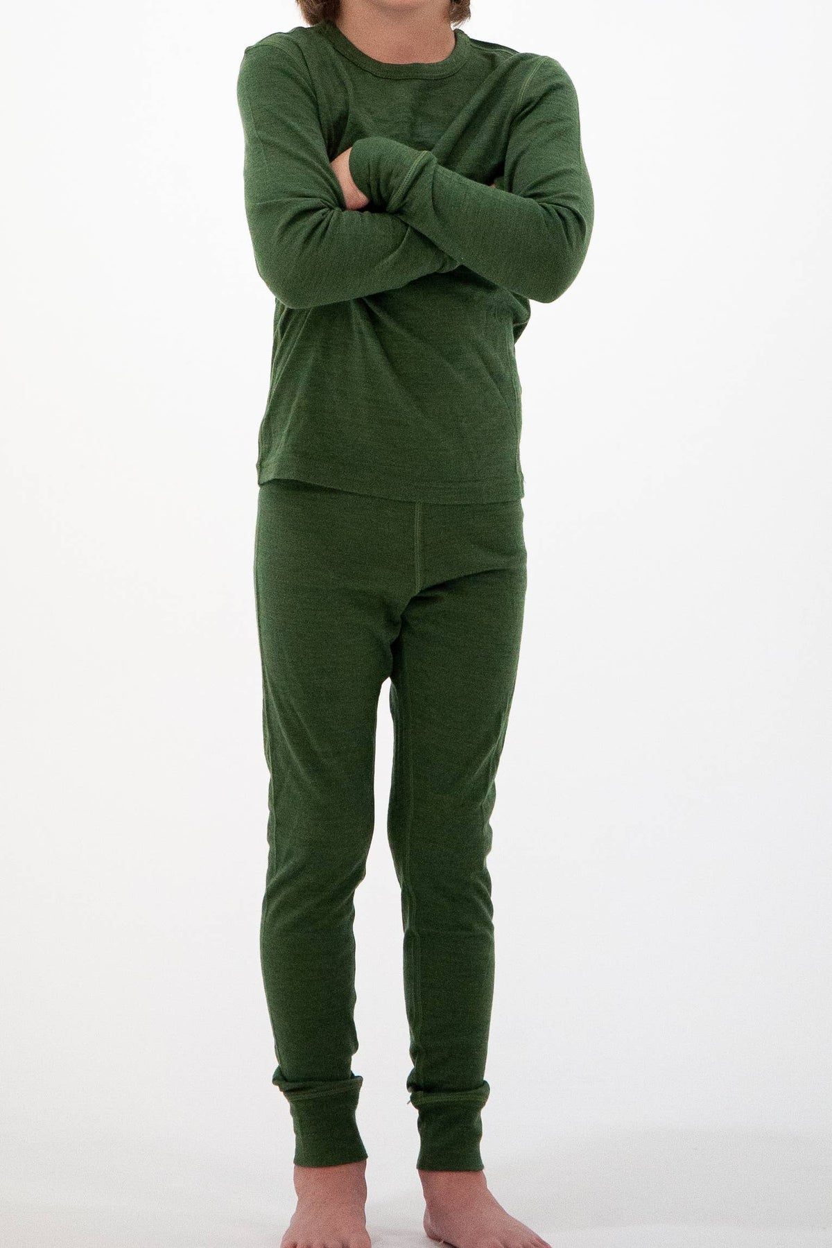 A child wearing a matching dark green long-sleeve top and pants set, standing with arms crossed against a plain white background.