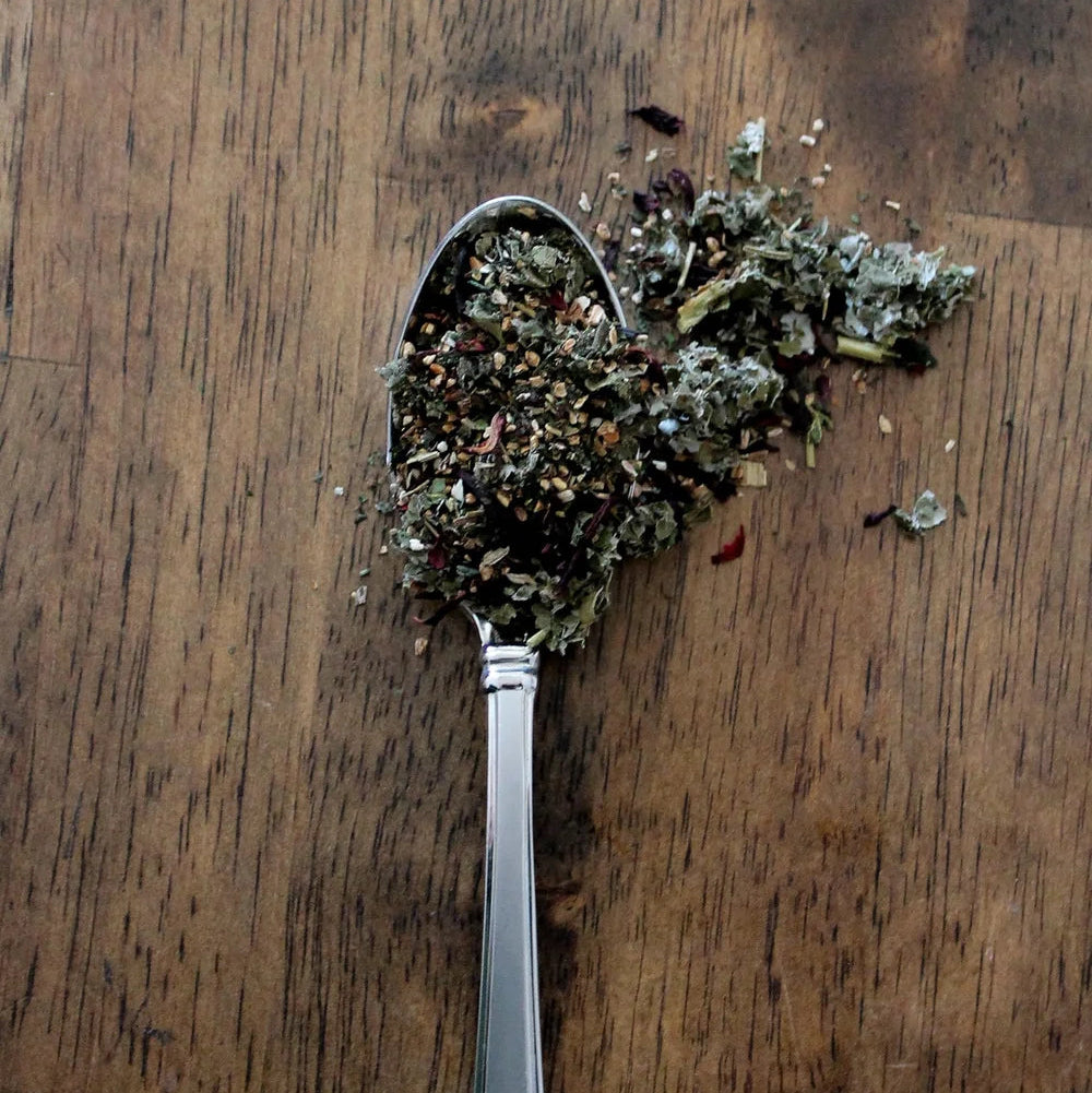 Silver spoon filled with dried herbs on a wooden surface