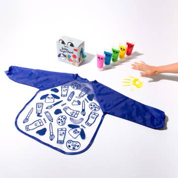 Blue apron with drawings on a white surface, with a box of crayons and a hand holding a yellow crayon.