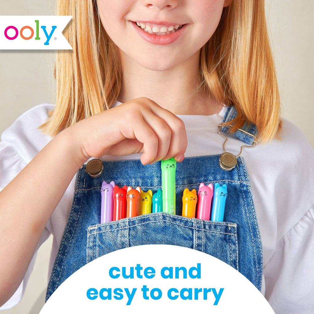 A young girl with blonde hair wearing blue denim overalls and a white t-shirt, holding a green pen in the front pocket of her overalls. Several colorful pens are tucked into the pocket.