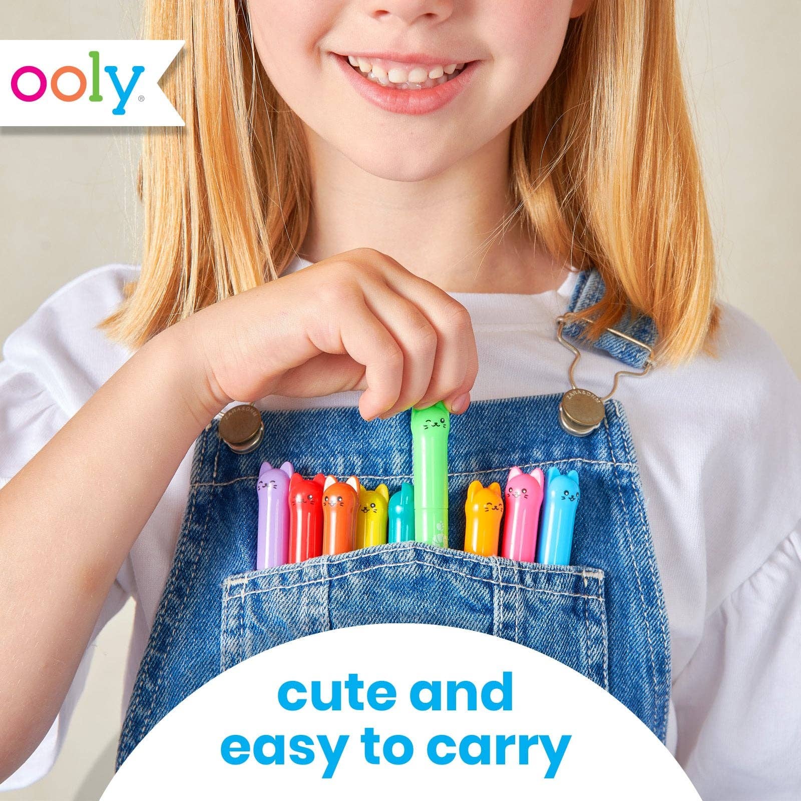A young girl with blonde hair wearing blue denim overalls and a white t-shirt, holding a green pen in the front pocket of her overalls. Several colorful pens are tucked into the pocket.