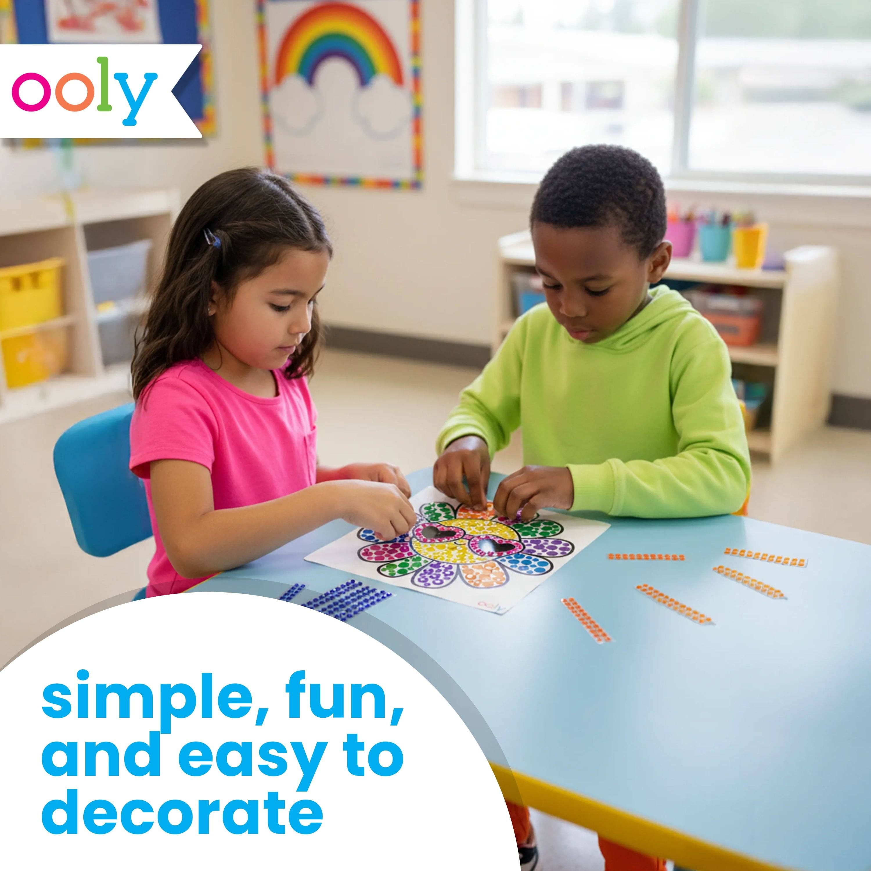Two children engaging in a craft activity with colorful materials in a classroom setting, featuring the Ooly brand.