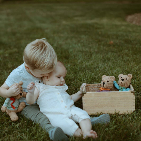 Two children playing with teddy bears on a grassy field
