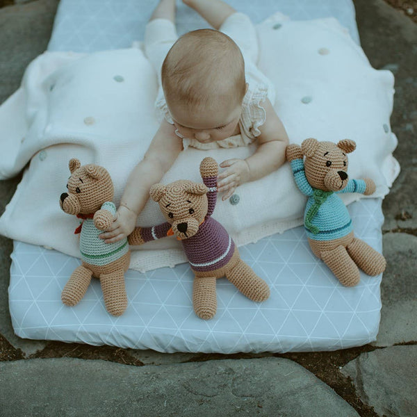 Baby playing with three teddy bears on a white blanket