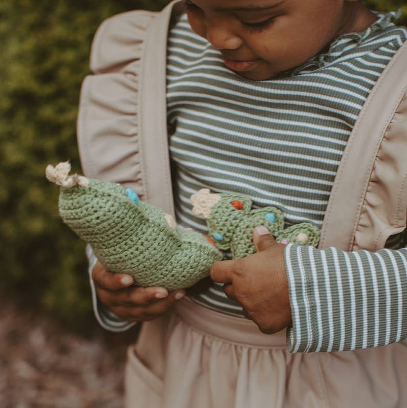 Child holding a green crocheted dragon toy outdoors