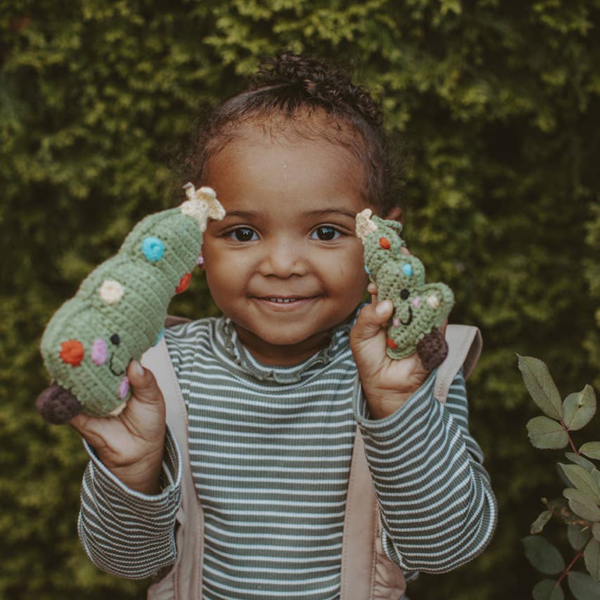 Child holding two green plush toys against a green leafy background