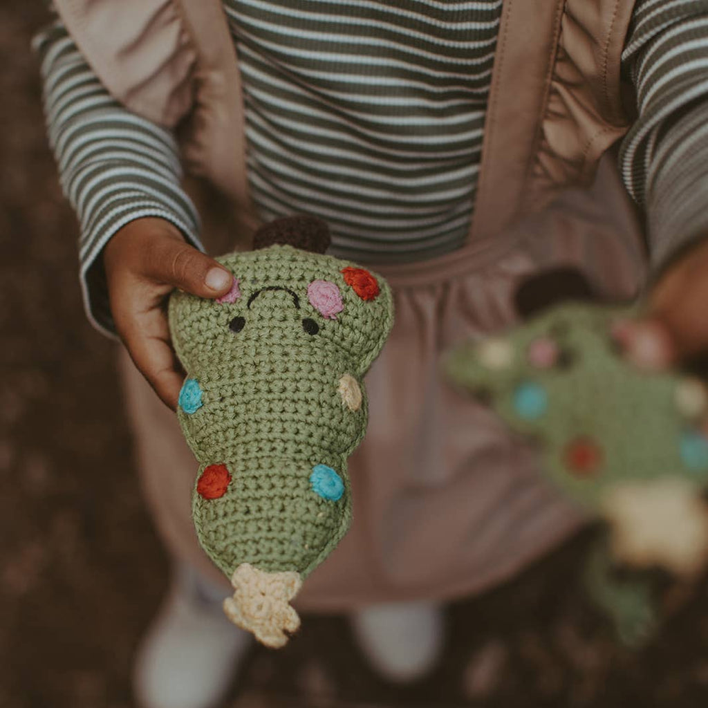 Child holding a crocheted toy with colorful flowers, wearing a striped shirt and brown overalls.