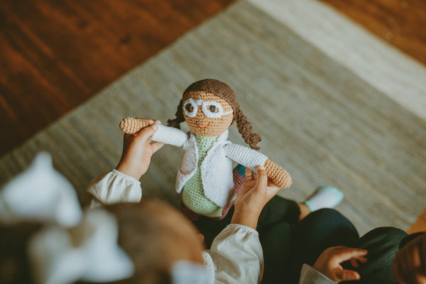Person holding a knitted doll with glasses on a wooden floor.