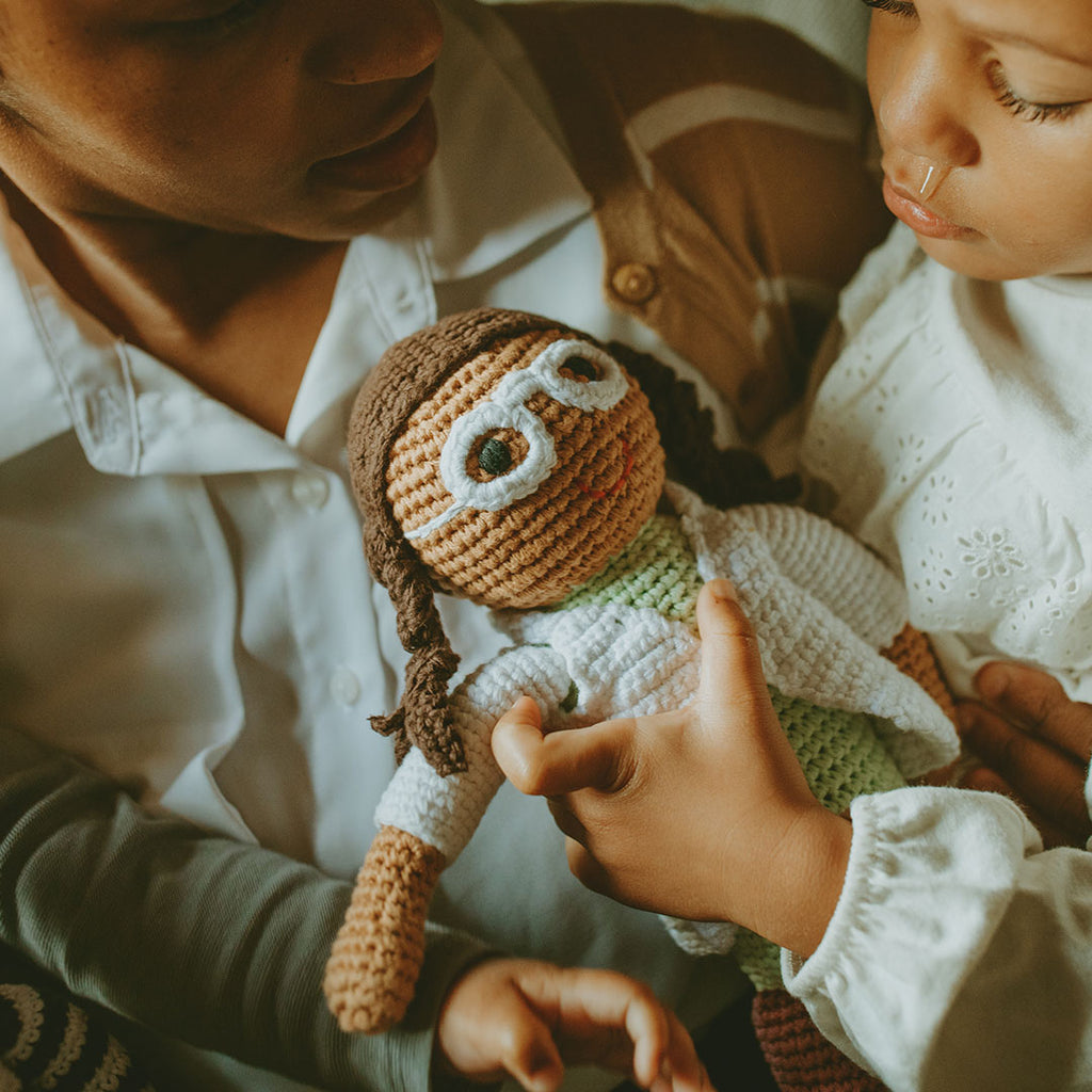Two children holding a knitted doll with braided hair and a green outfit.