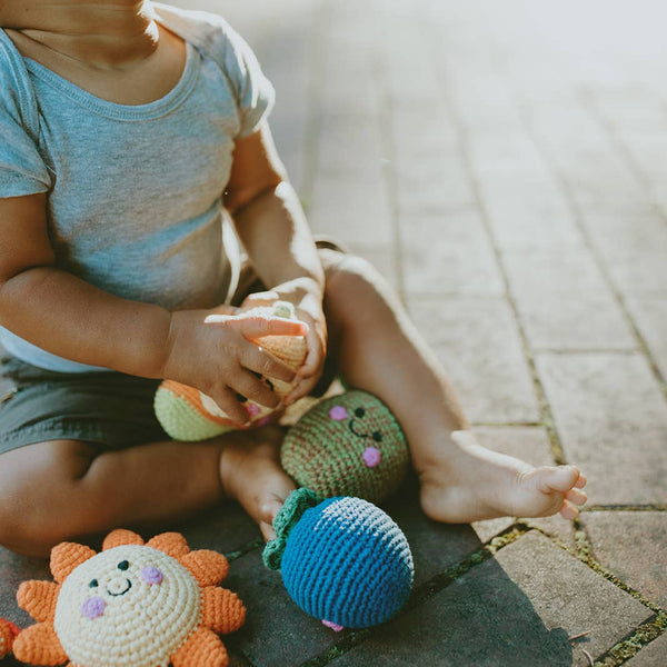 Child playing with colorful crochet toys on a stone pavement