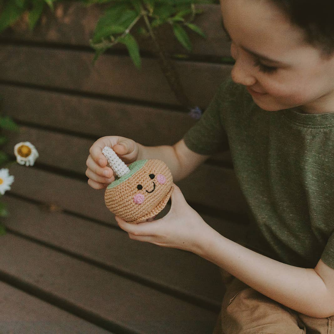 Child holding a small crochet pumpkin with a face against a wooden background