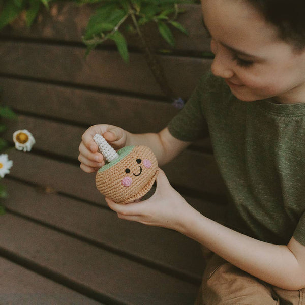 Child holding a small crochet pumpkin with a face against a wooden background