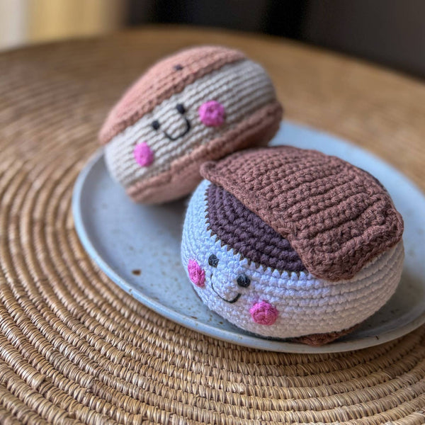 Two crocheted macaron toys on a small plate with a woven mat background