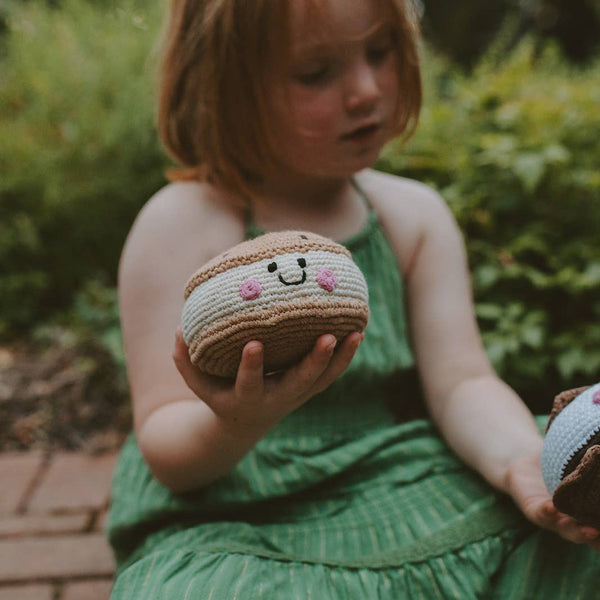 Child holding a crocheted macaron toy outdoors