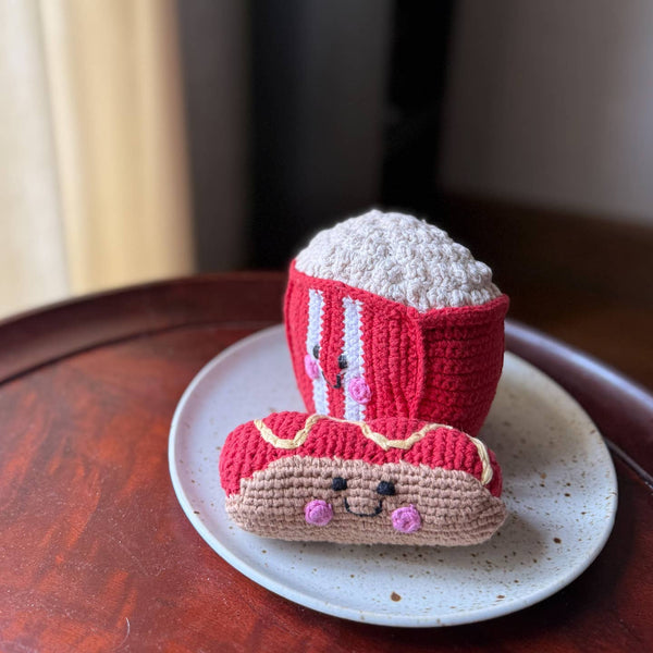 Crocheted hot dog with bun on a white plate on a wooden surface