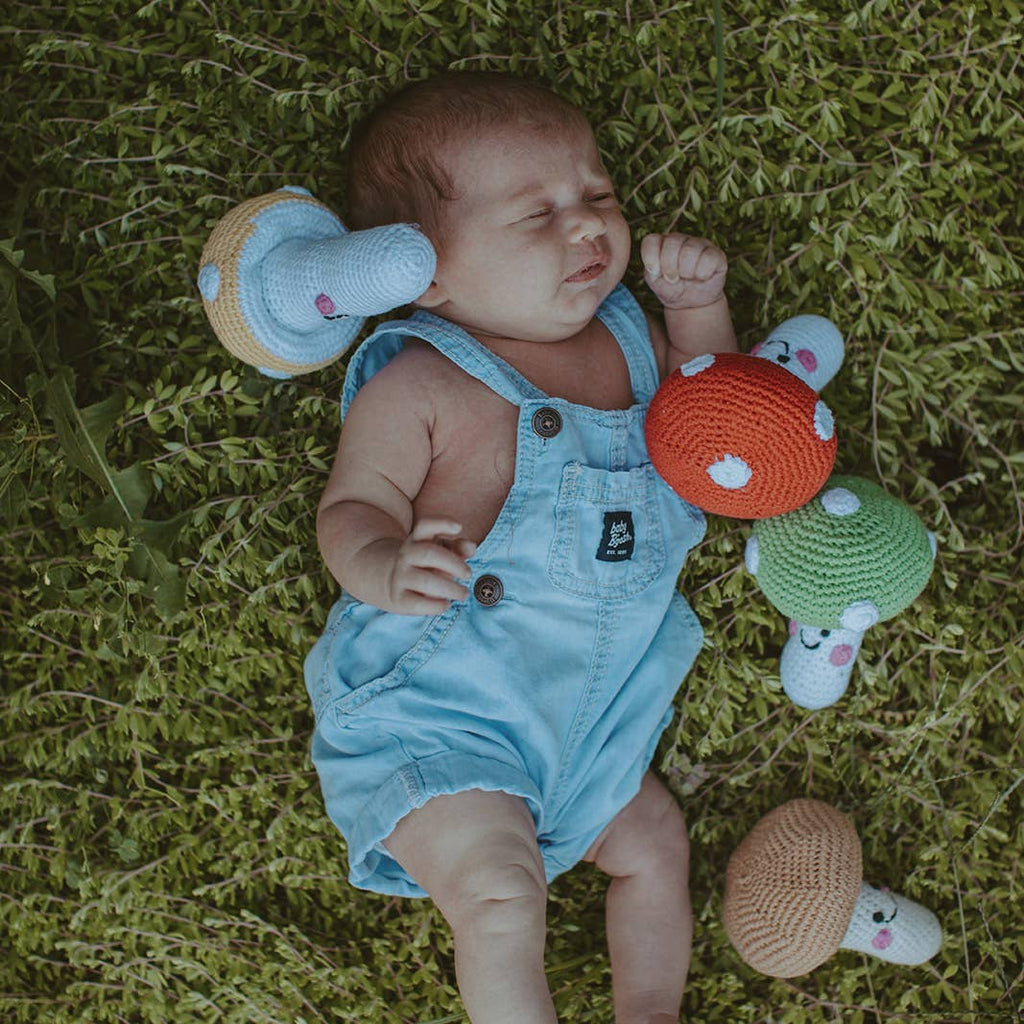 Baby lying on grass with colorful toys around