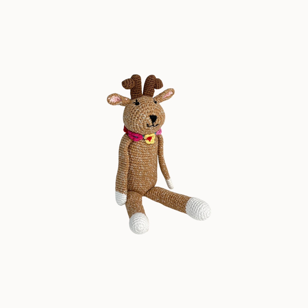 A handmade crocheted stuffed toy reindeer in brown yarn with white accents on its paws and feet, a pink collar, and a yellow bell, set against a plain off-white background.