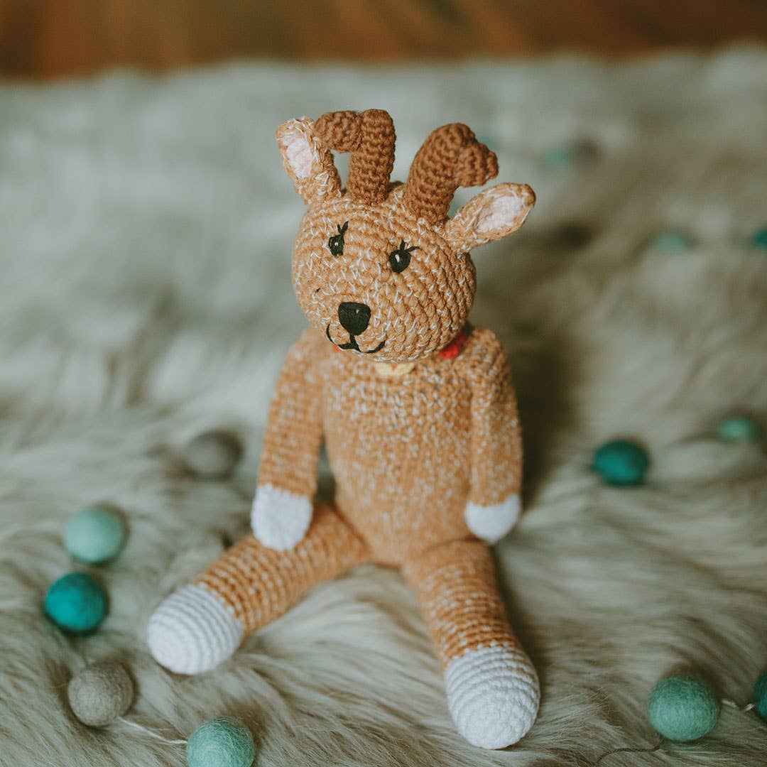 Knitted toy deer on a soft surface with teal balls around