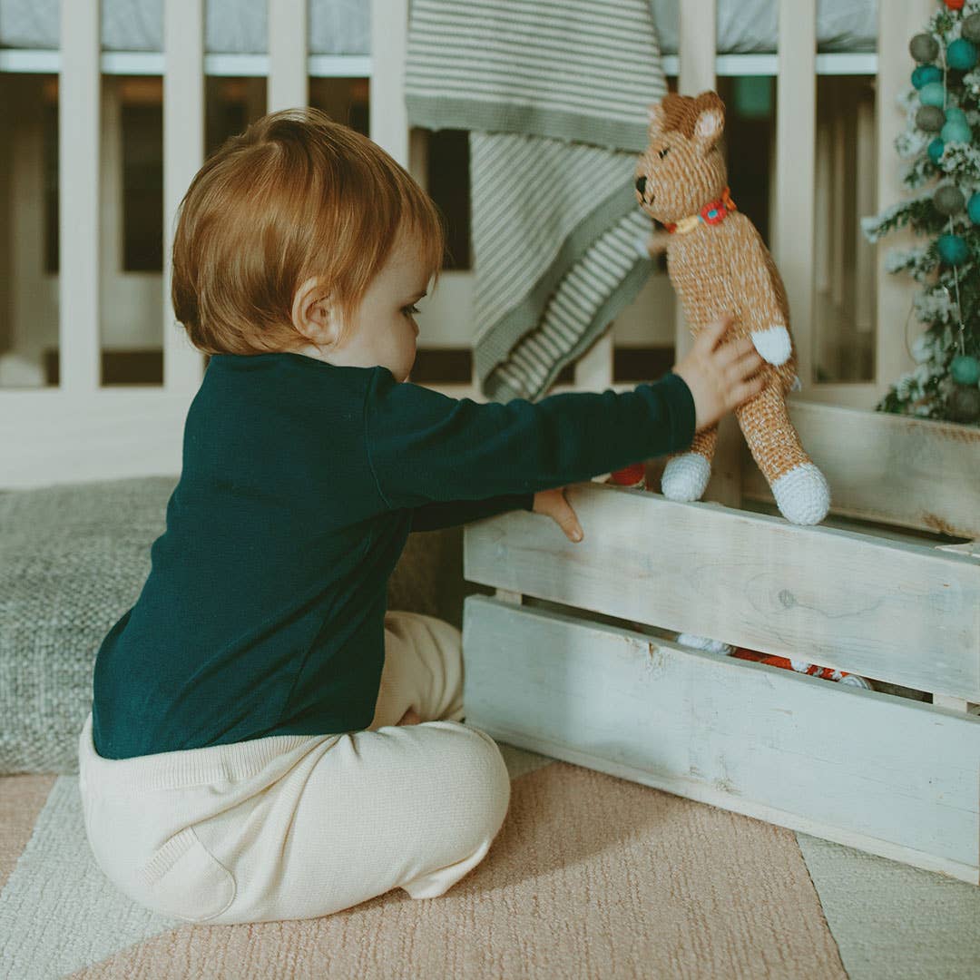 Child playing with a stuffed animal on a wooden crate in a home setting
