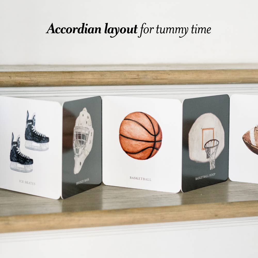 Accordian layout book for tummy time with sports-themed illustrations on a wooden surface.