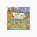 The front cover of the 'Cozy Creepy Cute and Relaxing Coloring Book' by Cherry Lam, featuring a Halloween-themed illustration of two white cats with black ears sitting among glowing jack-o'-lanterns in front of a house.