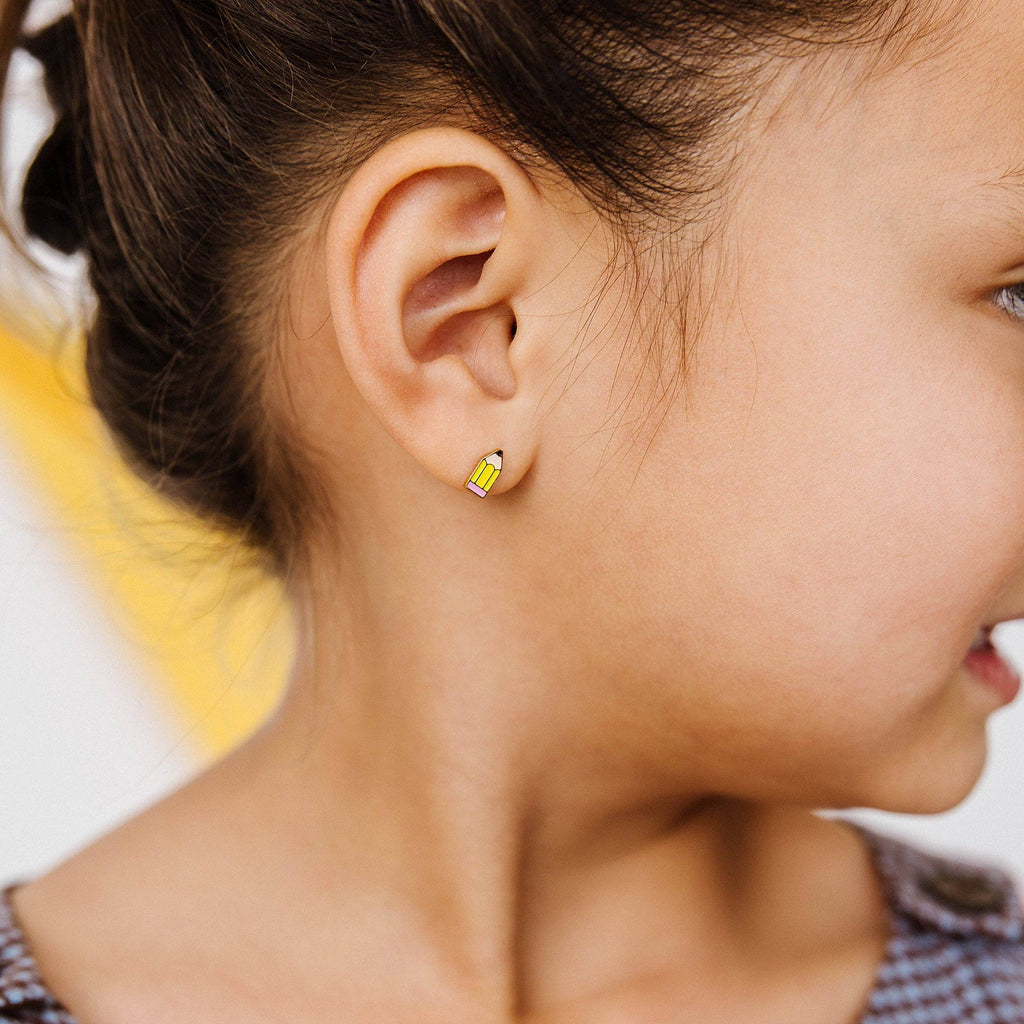 A close-up side profile of a young girl wearing a small yellow pencil-shaped stud earring.