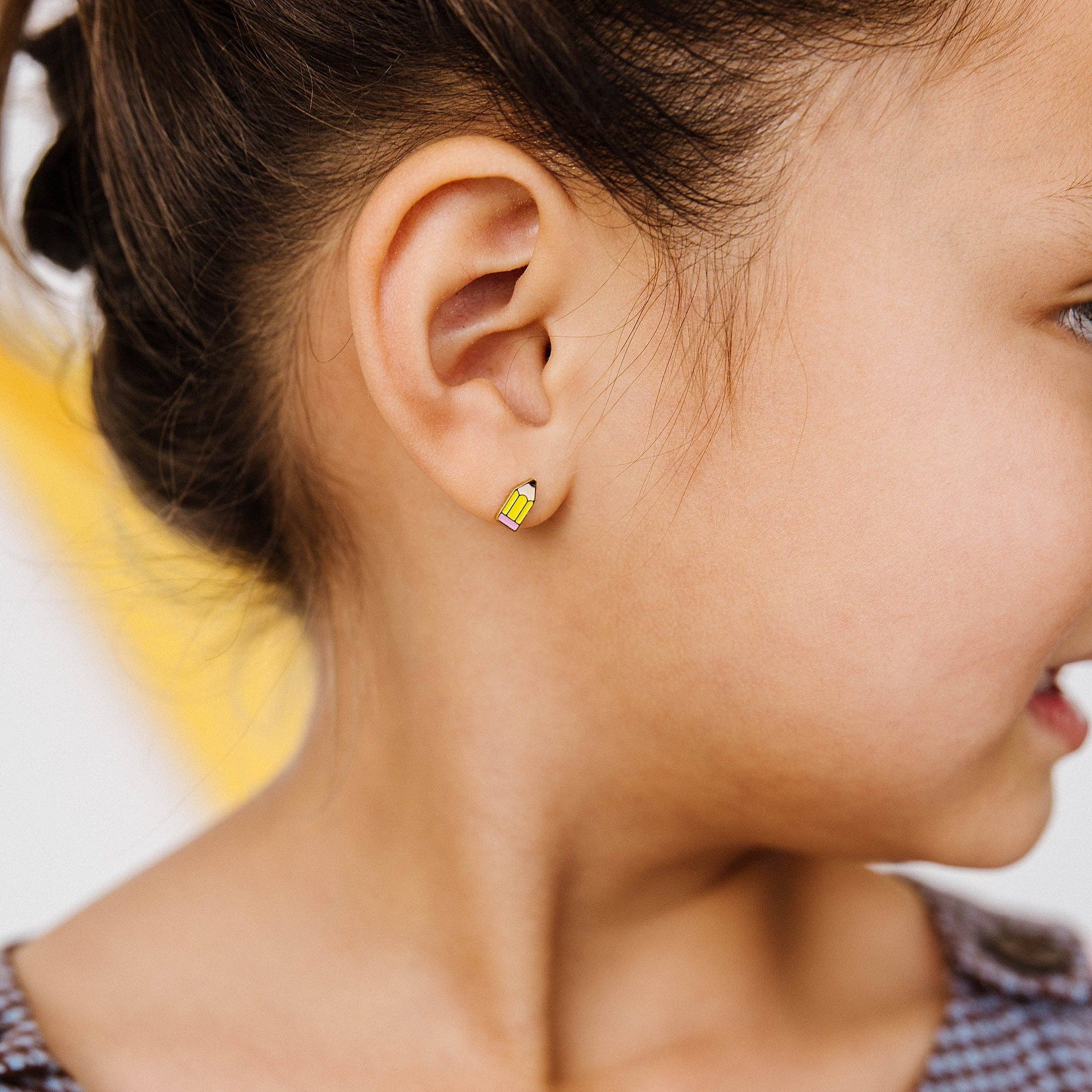 A close-up side profile of a young girl wearing a small yellow pencil-shaped stud earring.
