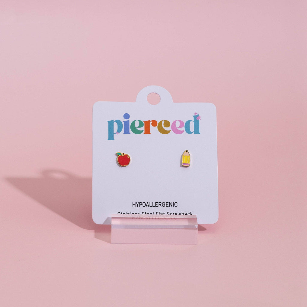 A pair of small colorful enamel pin earrings displayed on a white card labeled 'pierced' against a soft pink background.