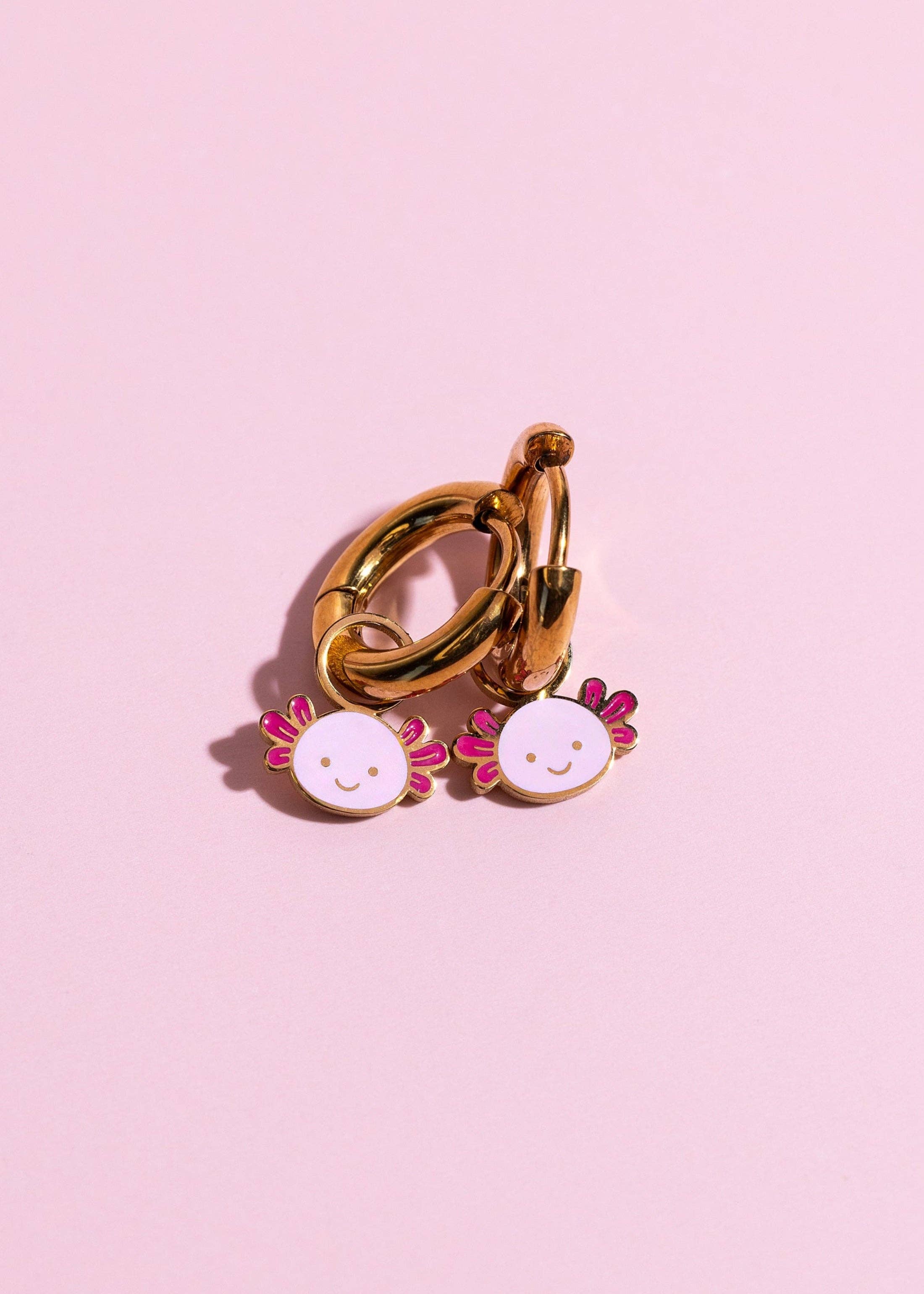 Gold ring with two small floral earrings on a pink background