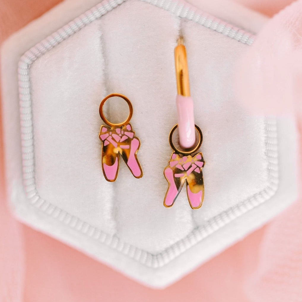 Ballet shoe earrings on a hexagonal white stand against a pink background