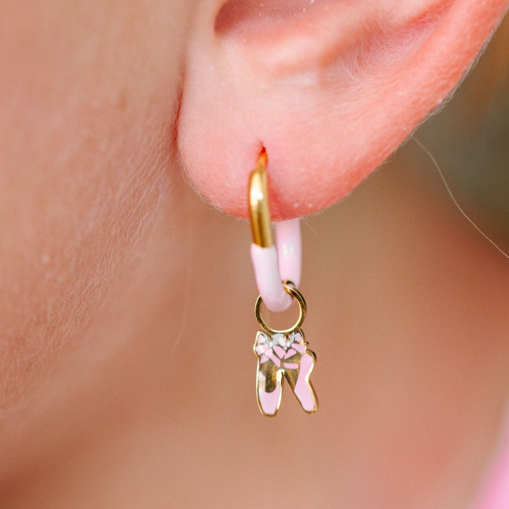 Gold hoop earring with a pink bow charm worn on an ear.