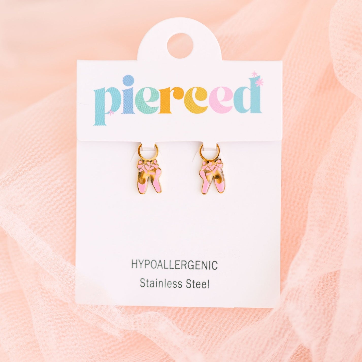 Pair of gold ballet slipper earrings on a 'pierceed' branded card with pink background