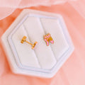 Pair of ballet shoe earrings in a hexagonal jewelry box on a soft pink background