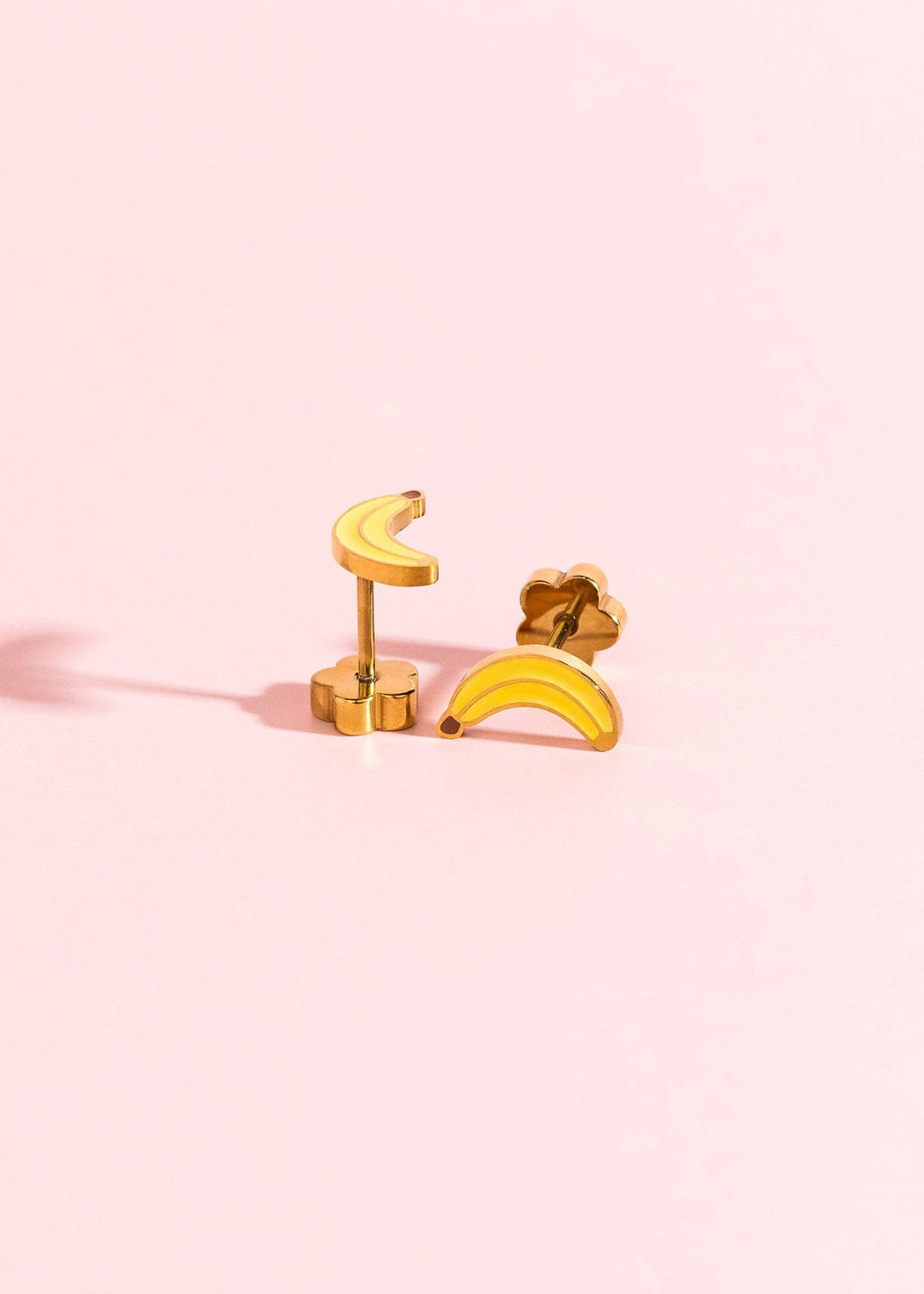 Gold banana-shaped earrings on a pink background