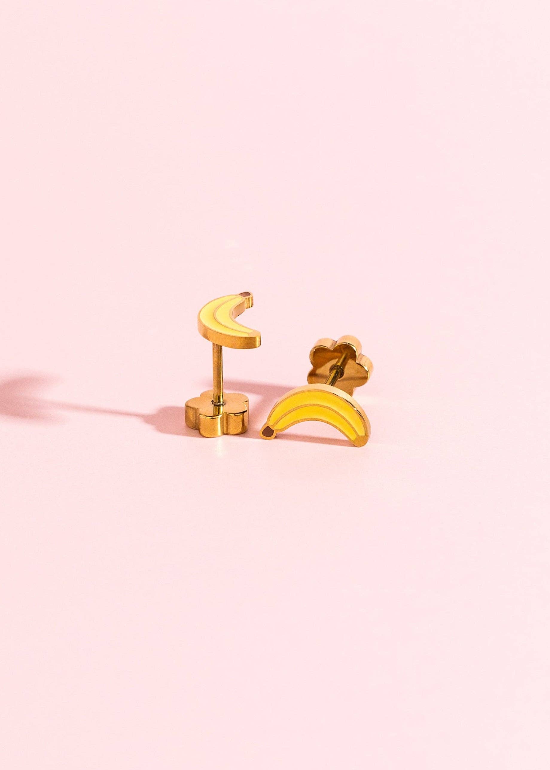 Gold banana-shaped earrings on a pink background