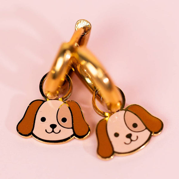 Gold hoop earrings with dog face charms on a pink background