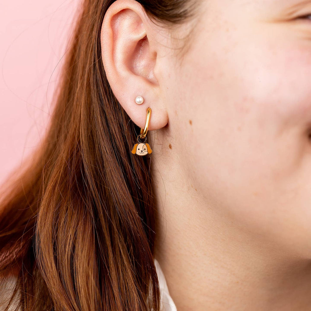 Close-up of a person wearing gold hoop earrings with a cat design against a pink background