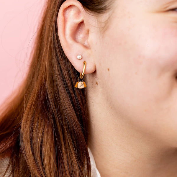 Close-up of a person wearing gold hoop earrings with a cat design against a pink background