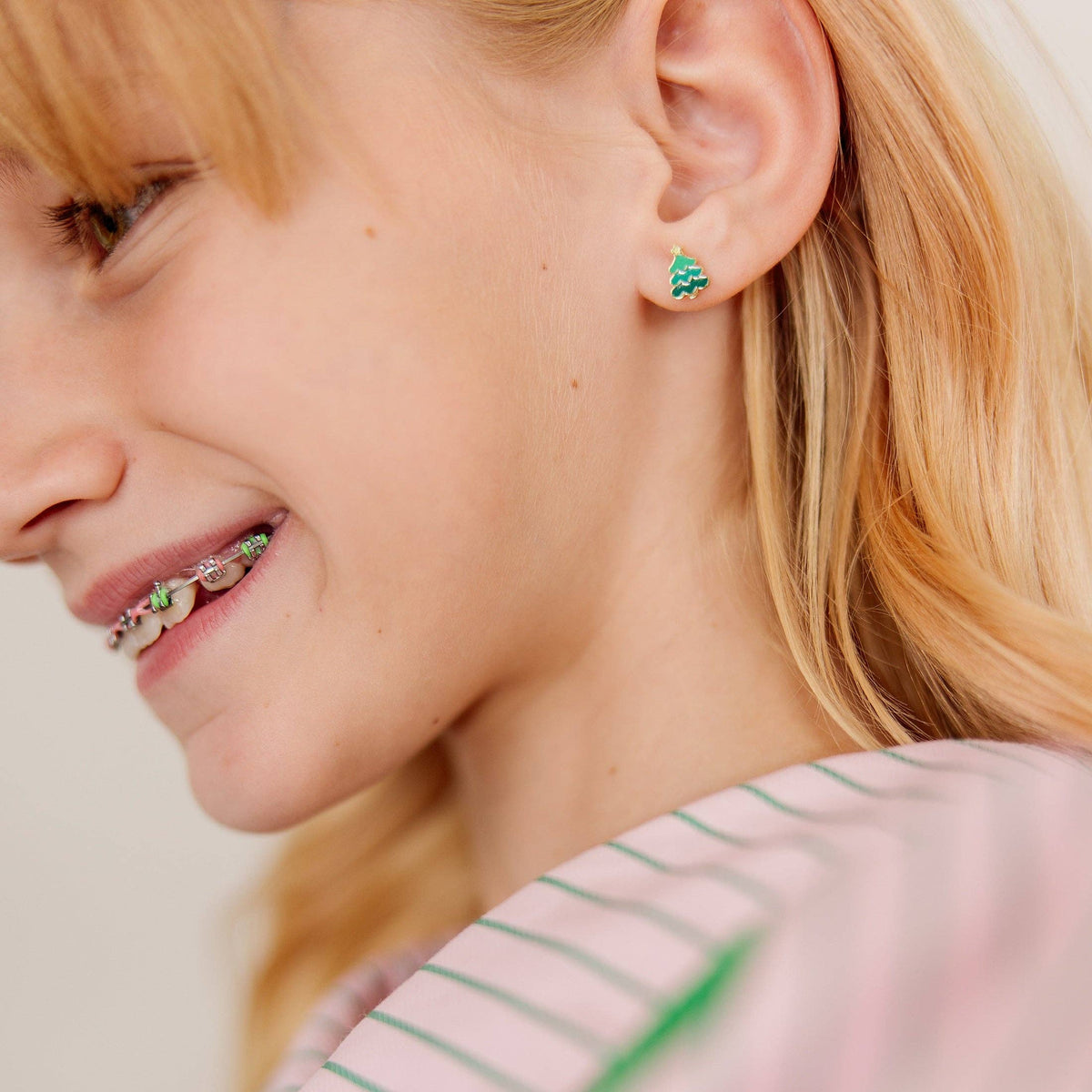 A close-up lifestyle shot of a young woman with blonde hair wearing a small green and gold textured stud earring.