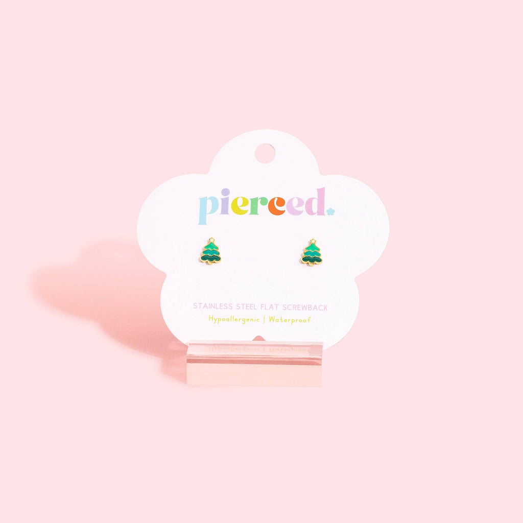 A pair of small Christmas tree stud earrings in green and gold, mounted on a white cloud-shaped card with the brand name 'pierce.' in colorful lowercase letters, displayed on a pink stand against a light pink background.