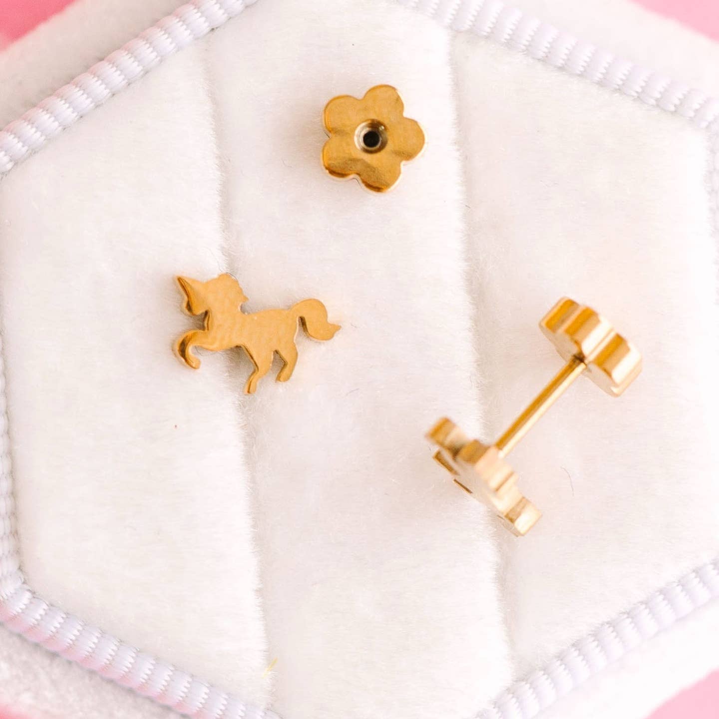 Gold unicorn-shaped earrings on a white cushion with a pink border