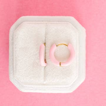 Pair of pink hoop earrings in a white jewelry box on a pink background