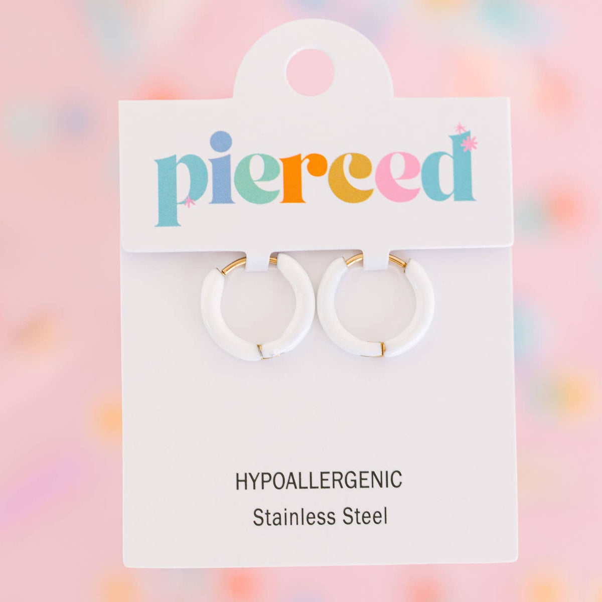 A pair of white hoop earrings with small gold accents, displayed on a white card labeled 'pierced' with text reading 'HYPOALLERGENIC Stainless Steel' against a soft pastel blurred background.