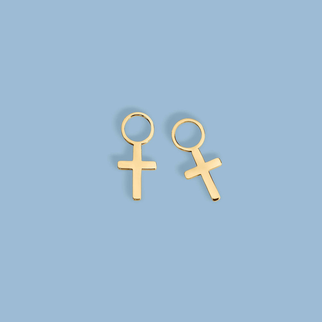 A pair of gold-plated cross stud earrings with a flat, polished cross design and a circular top loop, shown on a clean blue background.