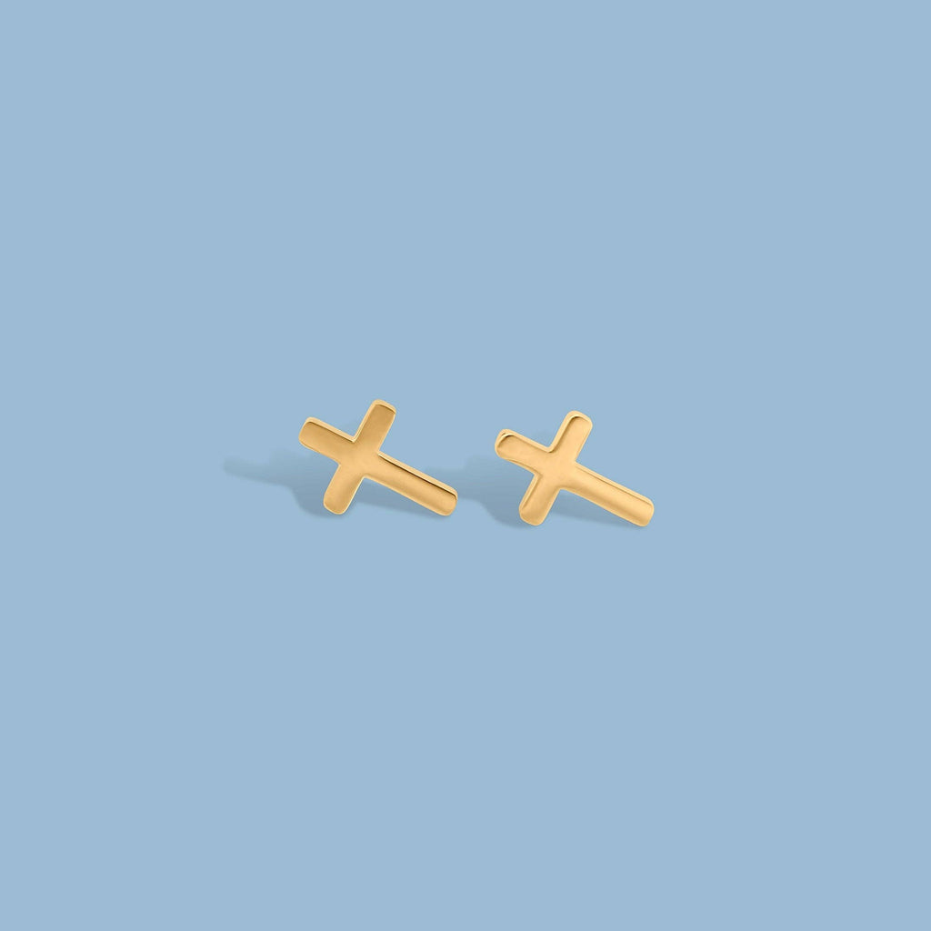 A pair of small gold cross stud earrings on a plain blue background.