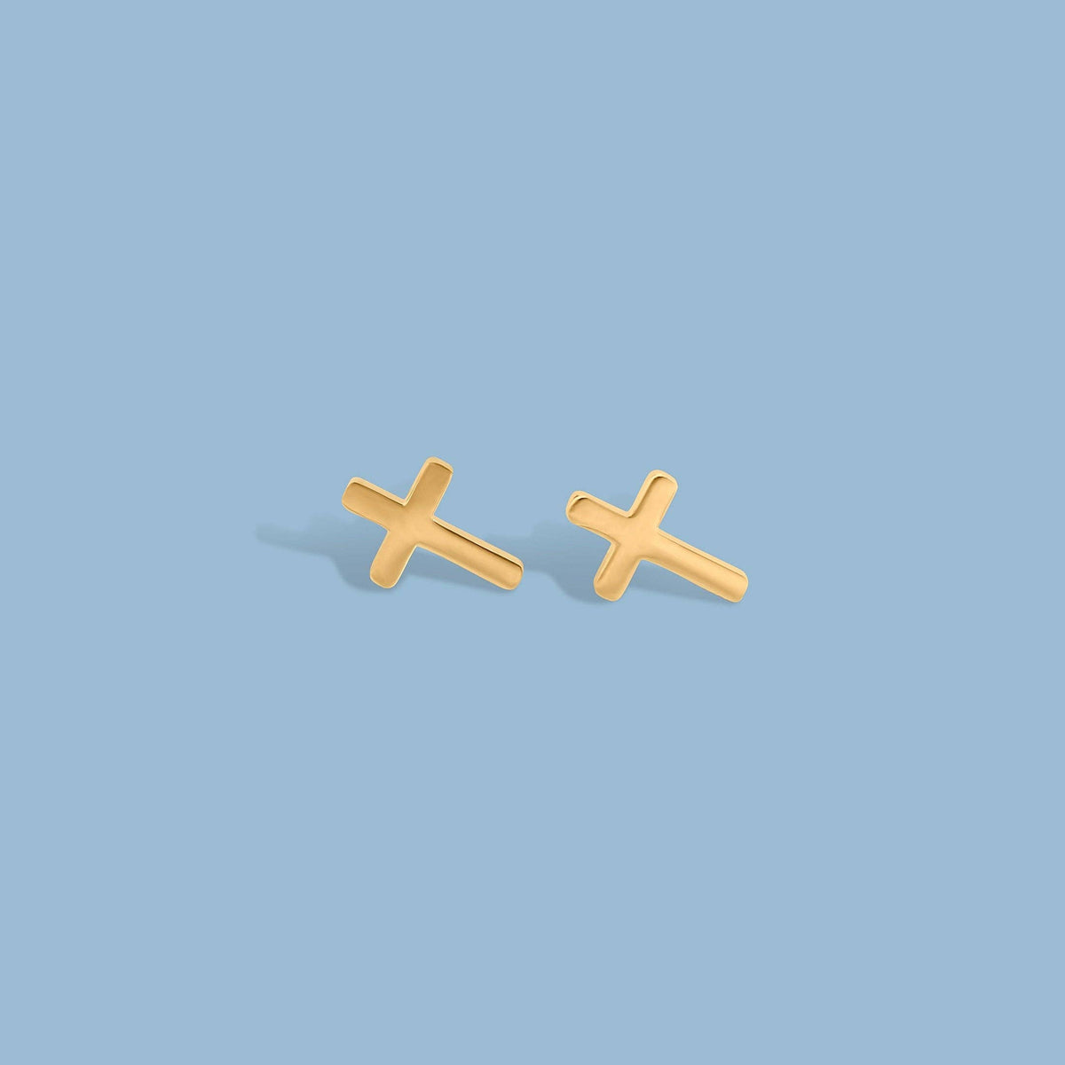 A pair of small gold cross stud earrings on a plain blue background.