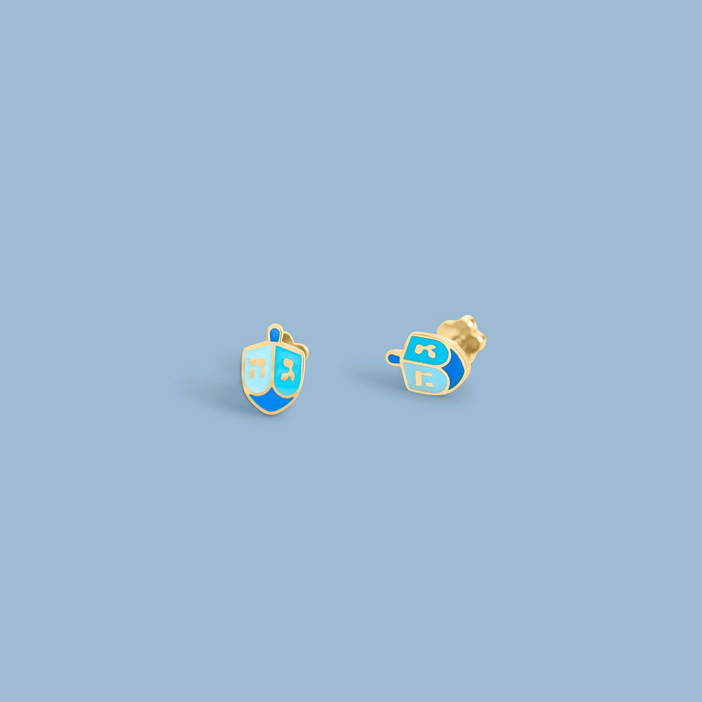 A pair of gold-tone stud earrings shaped like a dreidel, featuring light blue and royal blue enamel sections with gold lettering, shown on a plain blue background.
